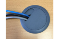 Cables going through a grey plastic desk cable tidy grommet in wooden desk.