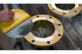 Black self adhesive disc having liner peeled away by hand with flange in the background.