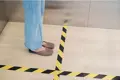 Person standing on marked off area of floor demonstrating hazard warning tape.