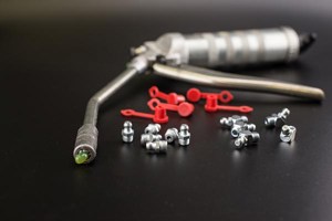 Grease gun with metal grease nipples and red protective caps displayed on a black surface.