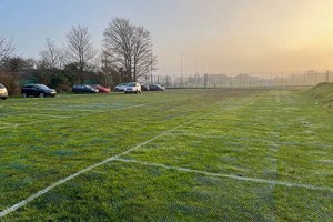 A temporary car park with grass growing through the plastic mesh and lines painted on top.