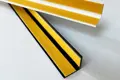 Two right angled plastic extrusions in white and black. With Self adhesive tape fitted to both internal faces.