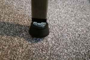 A black plastic threaded square tube insert with an adjustable foot attached. Fitted into a square metal tube. Standing up.