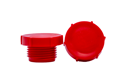 Two red plastic metric threaded plugs. One standing and one on its side.