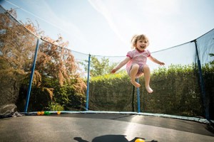 Child jumping on trampoline in a garden in the sunshine.